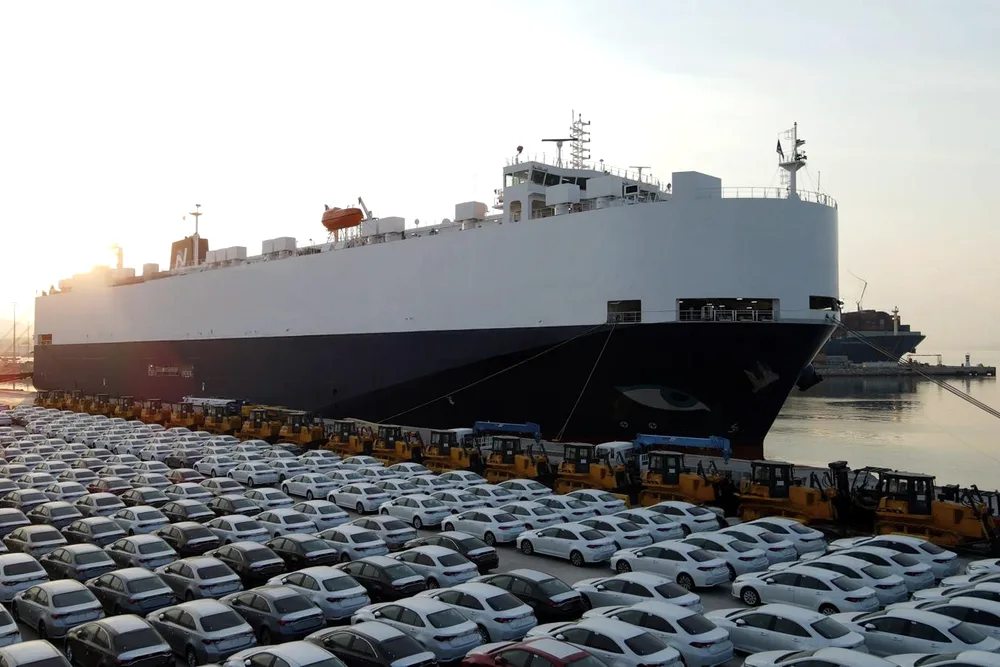 Car carrier at the quay, with new vehicles lined up in front of it for loading.